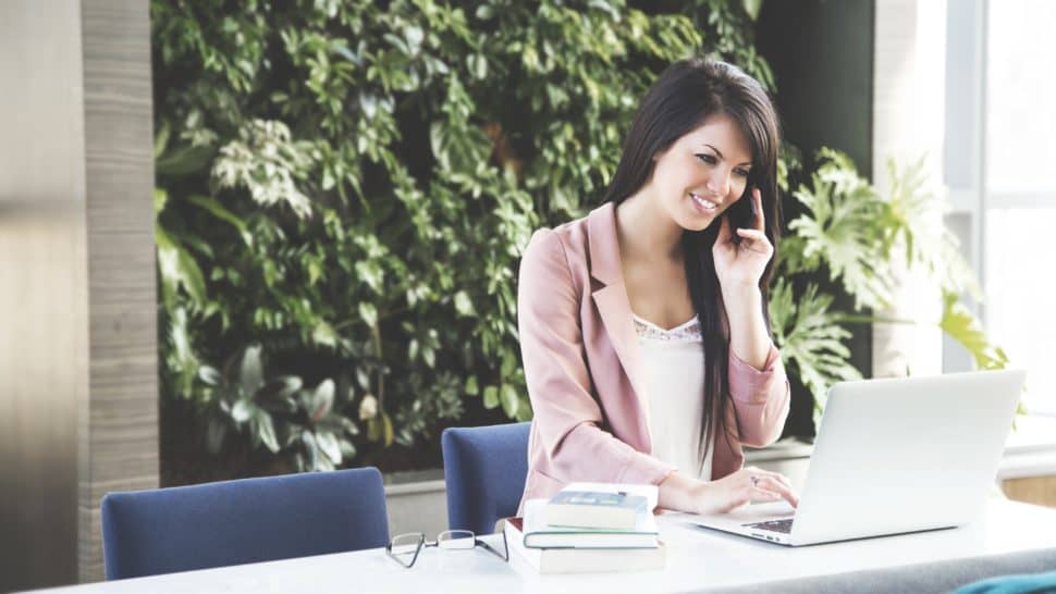 woman sitting working on laptop and talking on phone