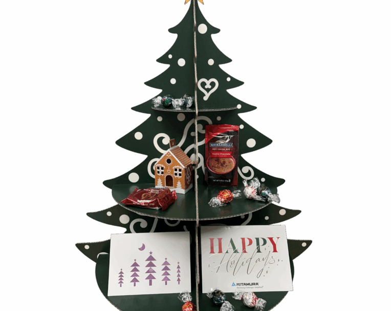 Green holiday tree display with die-cut cardboard shelves holding chocolates, cards, and a mini gingerbread house for festive gifting