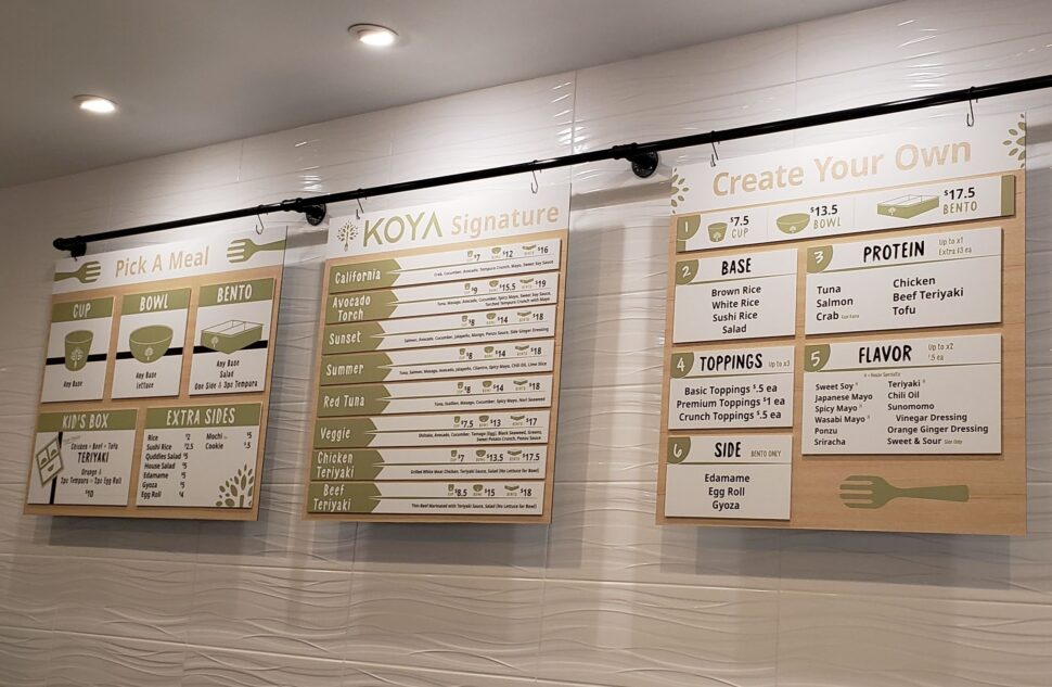 Hanging menu boards inside KOYA restaurant showing meal options, pricing, and customizable ingredients in a clean, modern layout