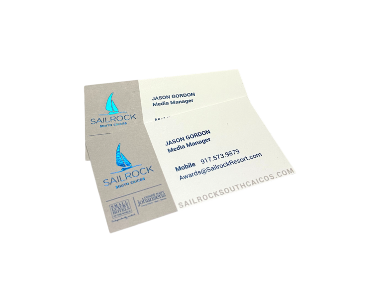 Custom blue foil business cards for Sailrock South Caicos resort showing a foil-stamped sailboat logo on pearl white card stock, front and back view