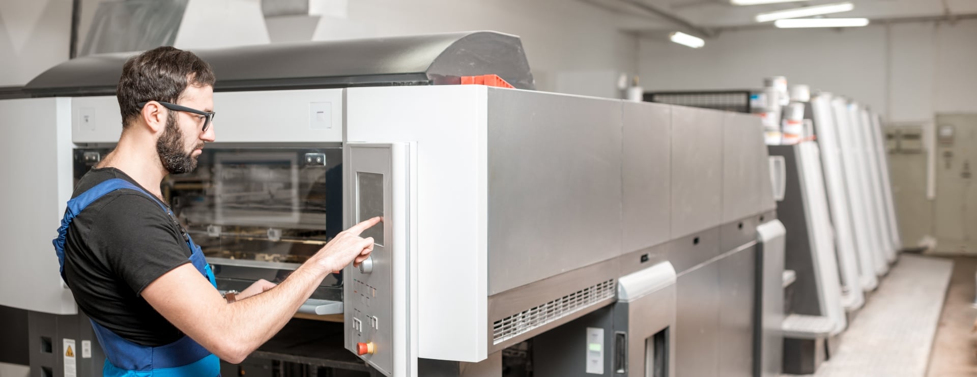 Press operator at the console of an offset press with the print units running behind him